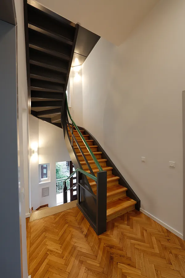 Saniertes Treppenhaus im Haus Olbrich mit dunkler Stahltreppe, Fischgrät-Parkett und moderner Wandbeleuchtung